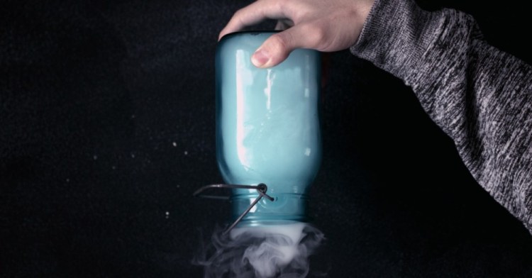 A man's hand holding a glass jar upside down and vapors and smoke are coming out of the mouth